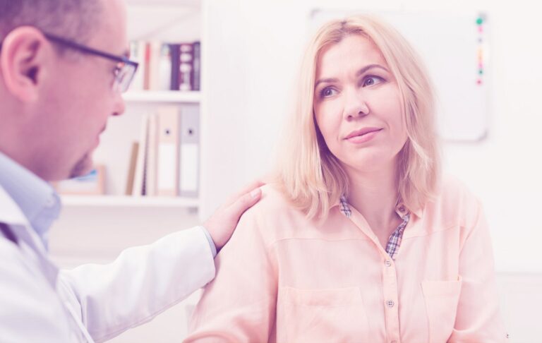 Arzt legt im Gespräch seine Hand auf die Schulter einer Patientin